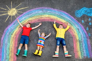 Drei Kinder liegen unter einem Regenbogen, den sie auf die Straße gemalt haben
