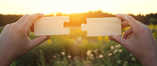 Hände, die zwei Puzzleteile zusammenführen