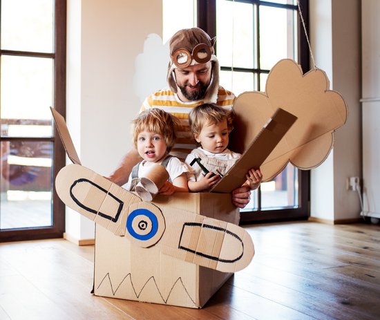 Ein Erzieher sitzt mit zwei Kindern in einem selbstgebauten Flugzeug aus Pappe