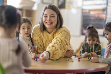 Eine pädagogische Fachkraft spielt mit Kindergarten-Kindern am Tisch