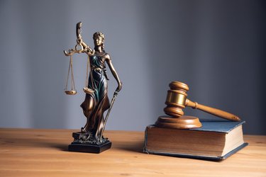 Die Figur der Justizia neben einem Gesetzbuch, auf dem ein Richterhammer aus Holz liegt