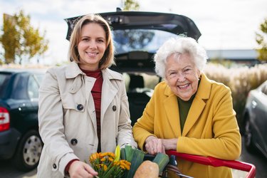 Weibliche Betreuungskraft mit einer alten Frau, die sich auf einen Einkaufswagen stützt