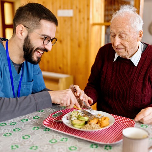 Eine männliche Pflegefachkraft hilft einem Senior beim Essen