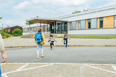 Laufende Grundschulkinder, die die Straße vor einer Schule überqueren