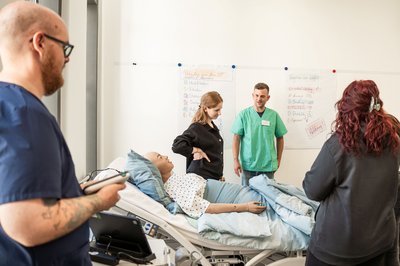 Ausbildungssituation in der Pflege: mehrere Menschen stehen am Bett mit Pflegesimulator