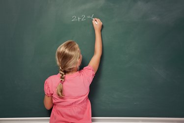 Blondes Mädchen mit Zopf und rotem Kleid löste eine Rechenaufgabe an der grünen Schultafel